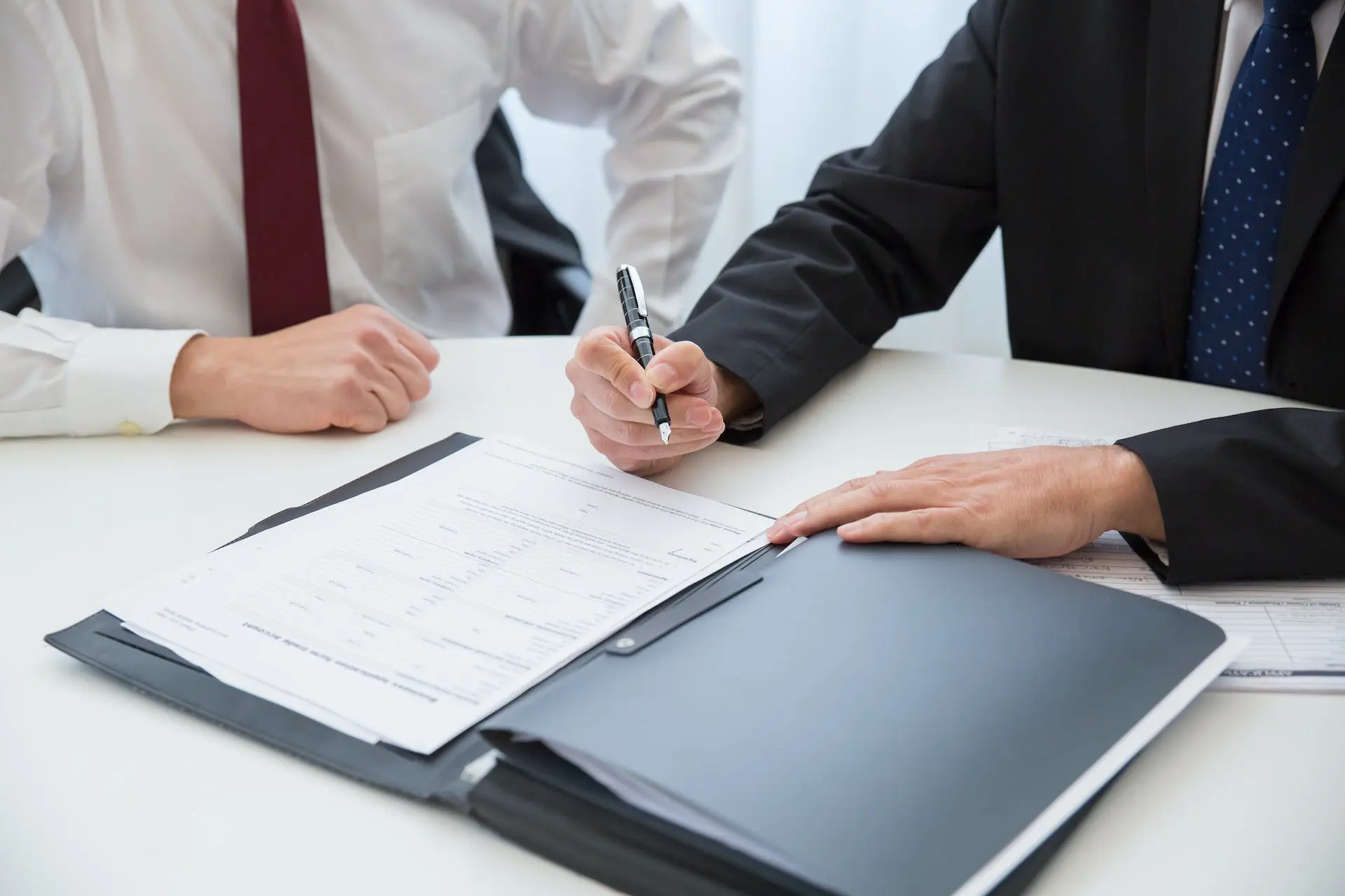 Two businessmen in suits reviewing and signing paperwork.