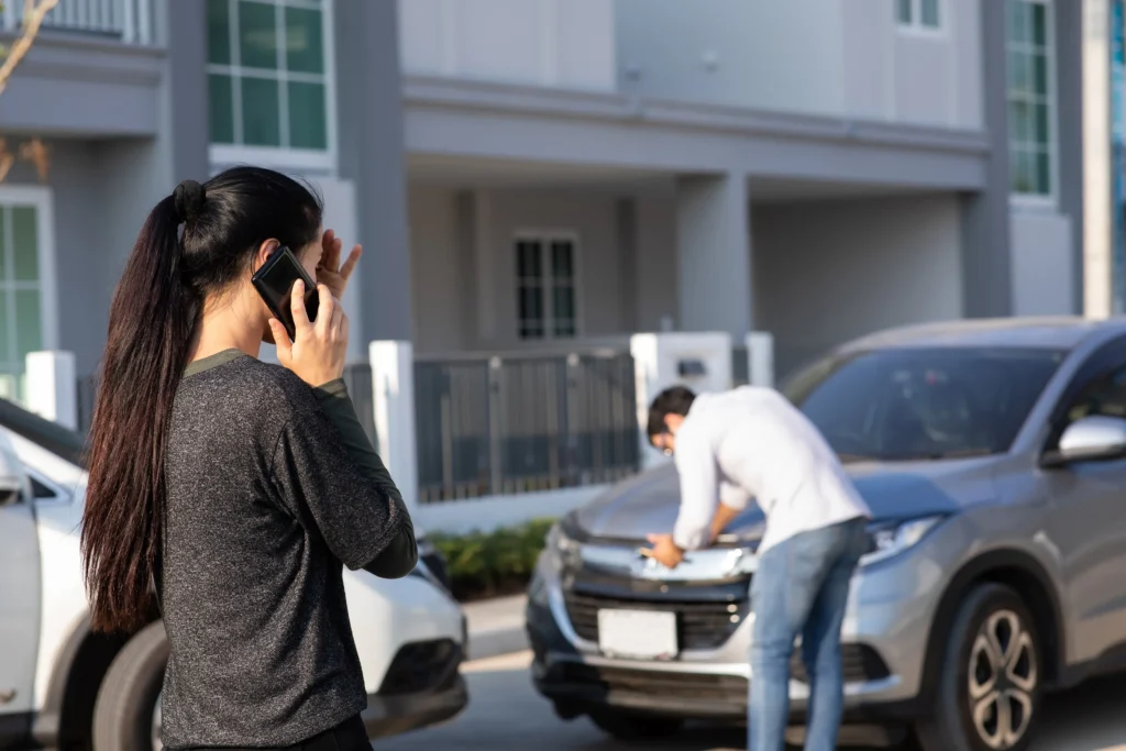 A woman and man inspecting their cars and calling 911 after a car accident.