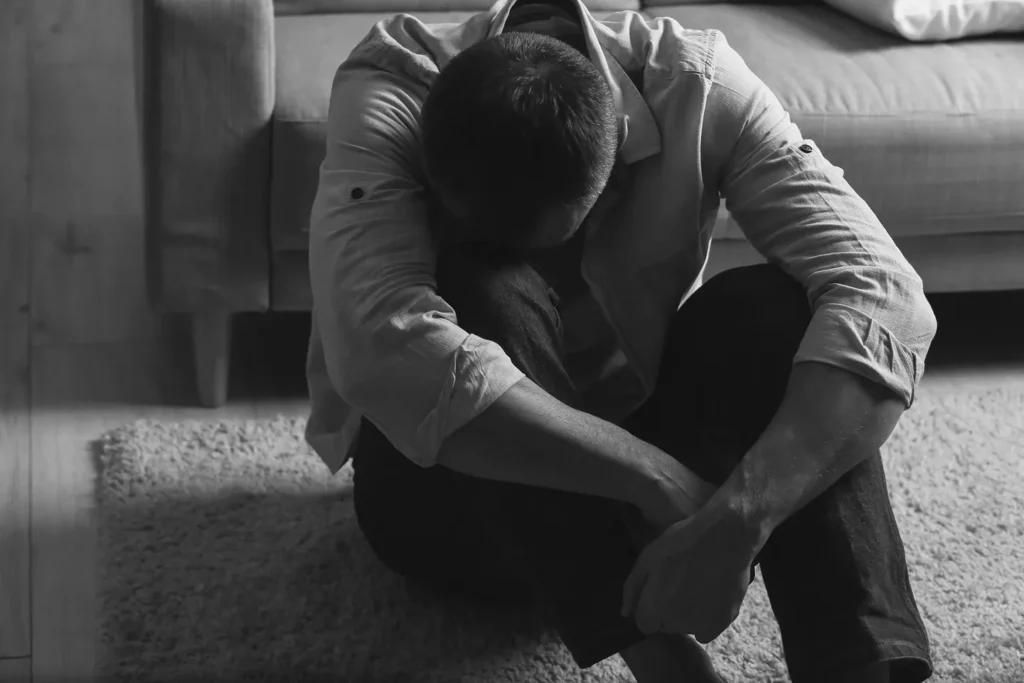 A distraught man hugging his knees.